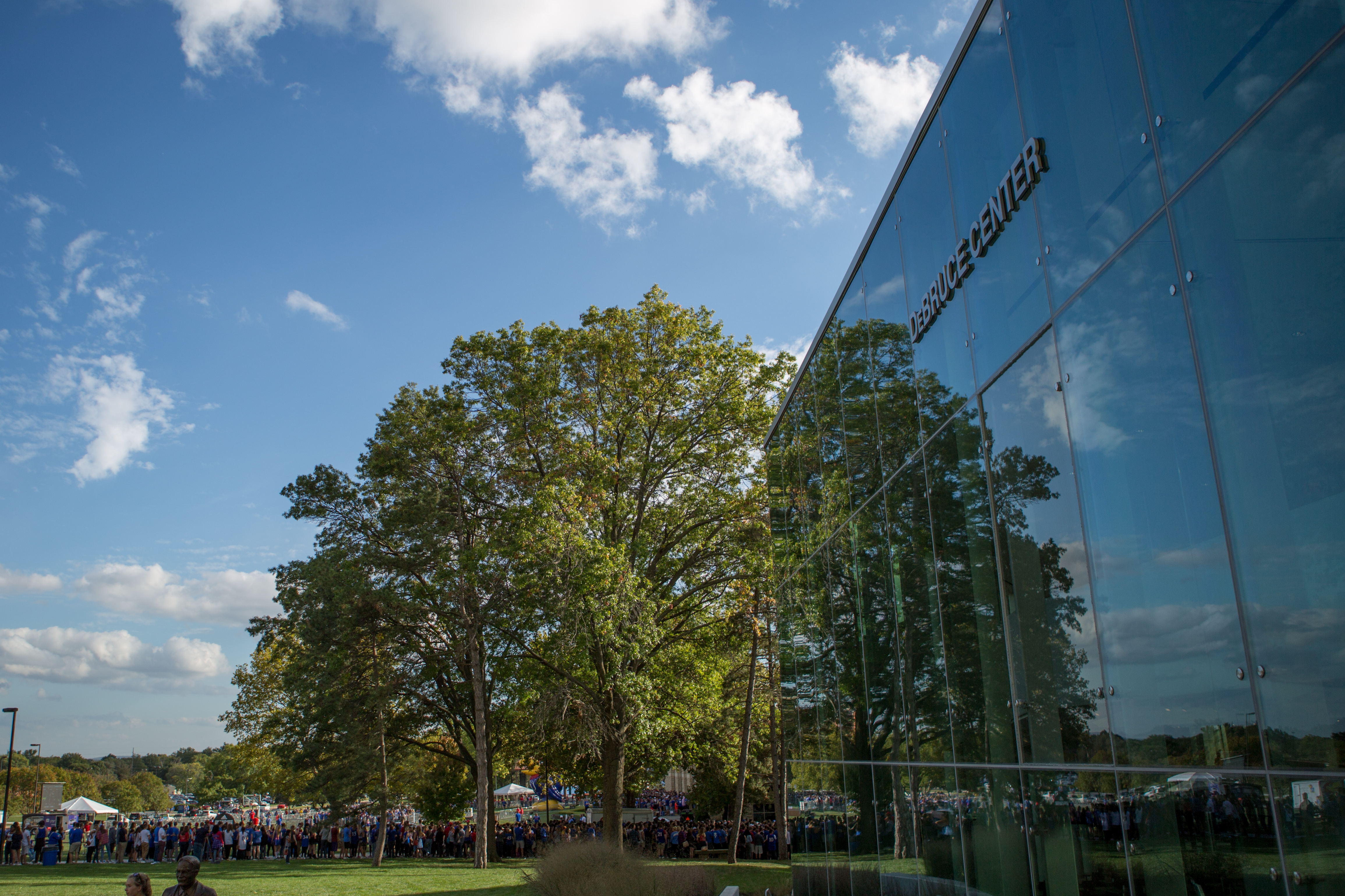 a tree, clouds, and a blue sky are reflected in the windows of the DeBruce Center