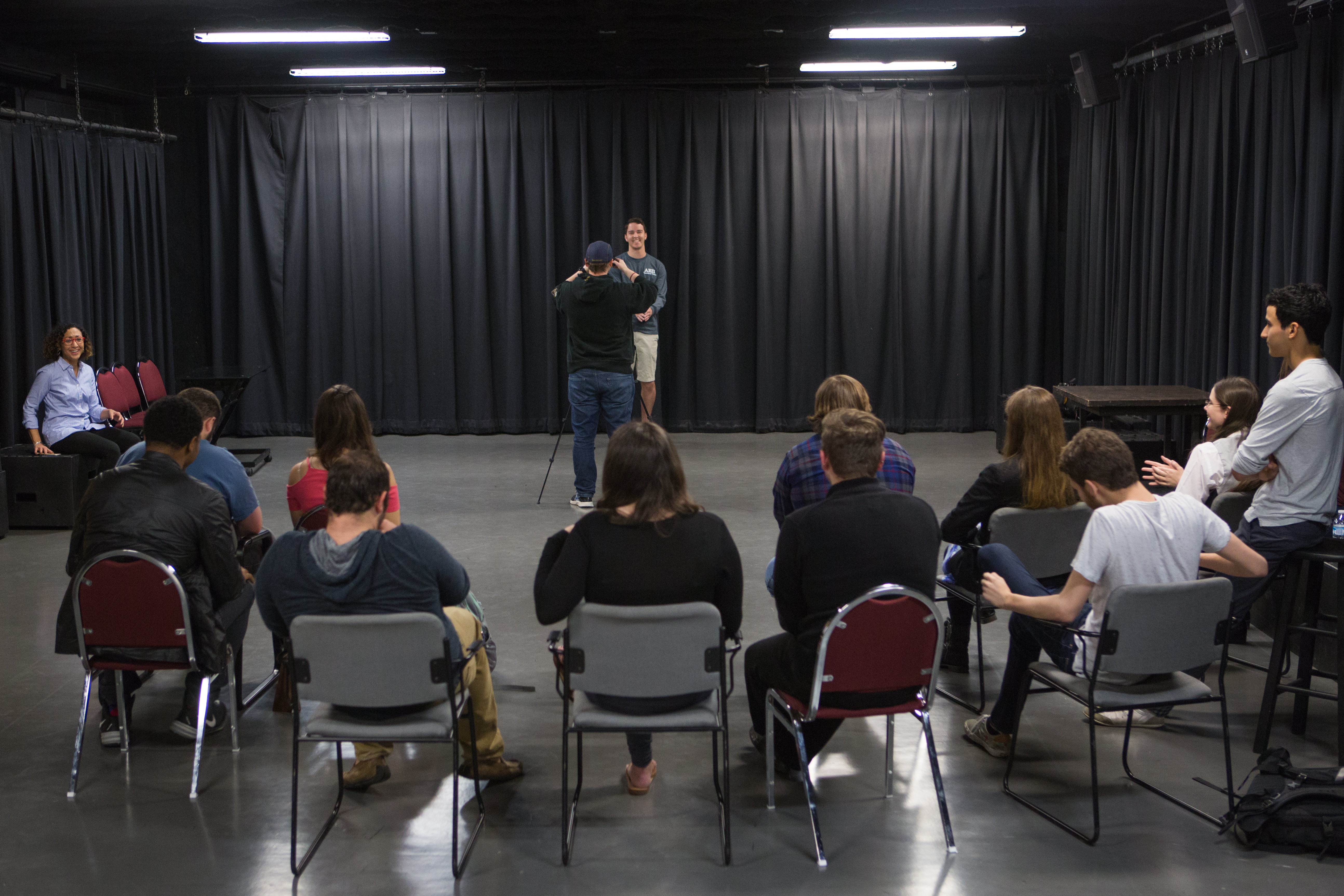 Students sitting in a semi-circle watching a student being photographed