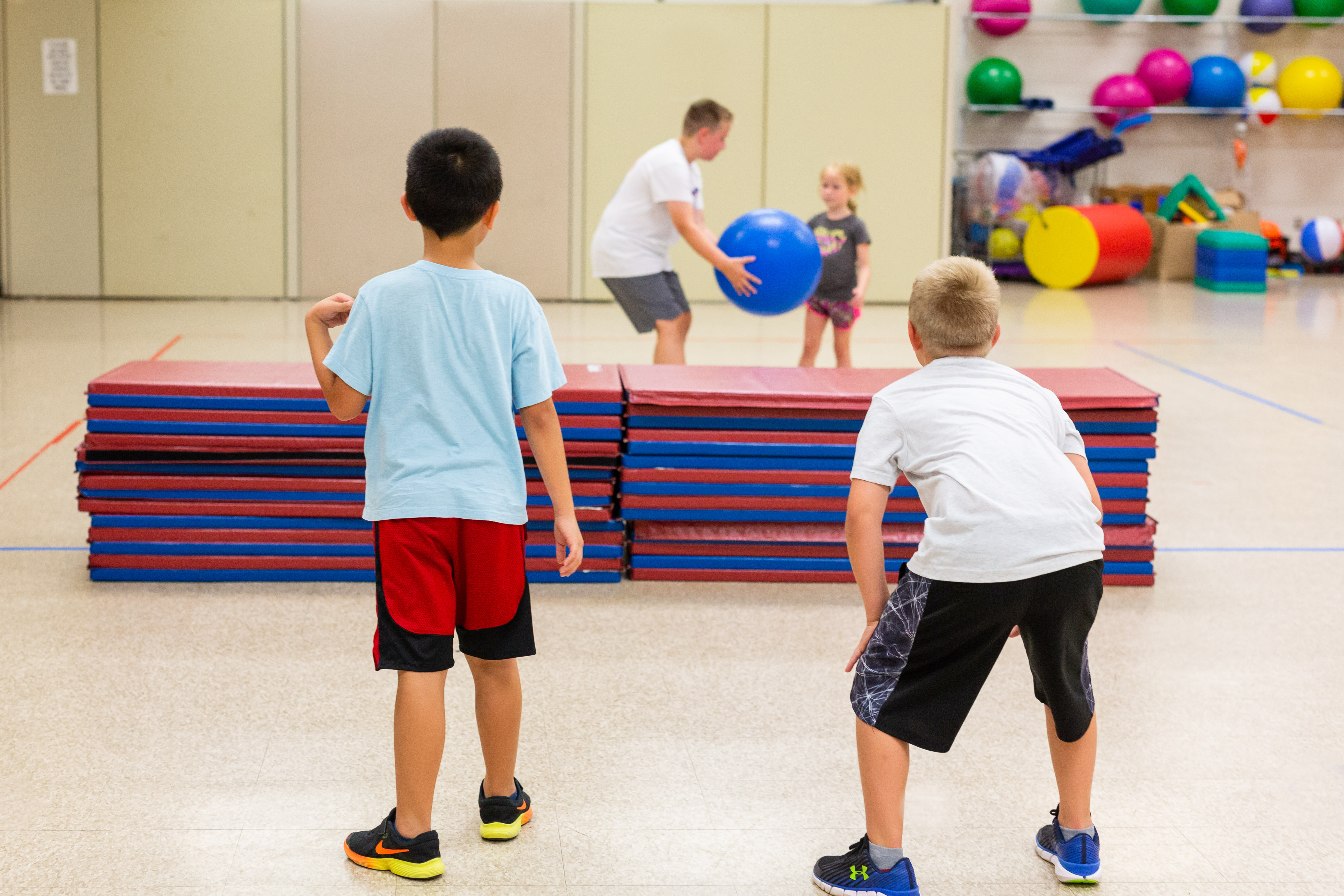 Three elementary school students and a coach play a game with an exercise ball