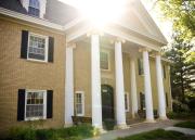 Sunlight peeks from behind Miller Scholarship Hall, a large, columned residence on KU campus