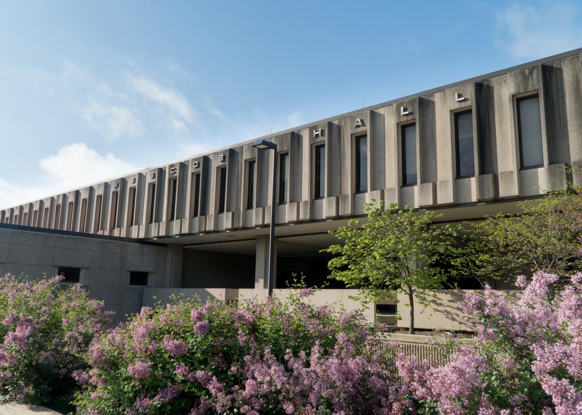 An exterior photograph of Wescoe Hall, with lilacs blooming in front