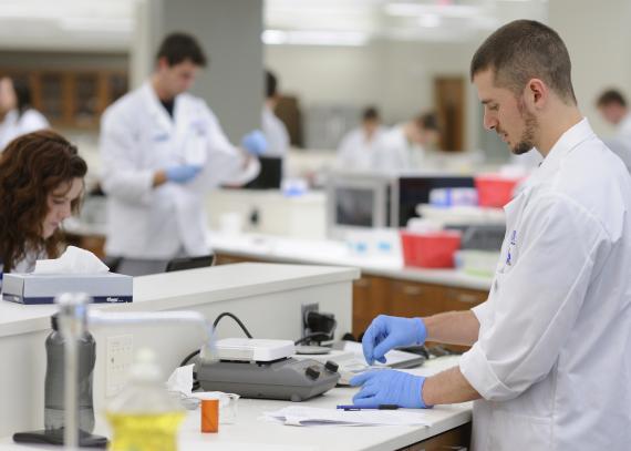Students in white coats work in a pharmaceutical laboratory