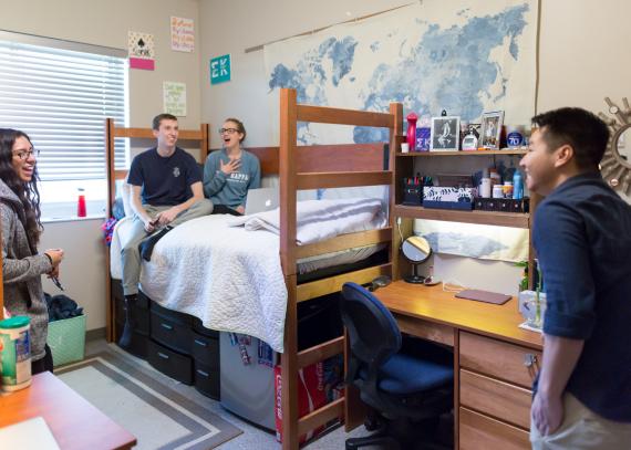 Four people talk and laugh in a student room in Self Hall