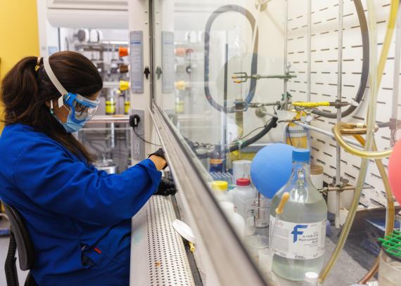 A woman wearing safety goggles conducts research in a pharmaceutical chemistry lab