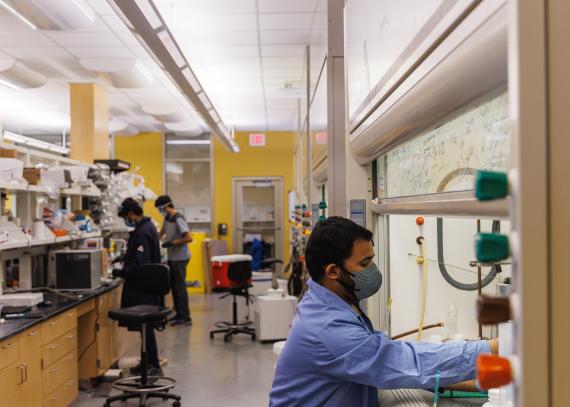 Three people work at different stations in a pharmaceutical chemistry lab