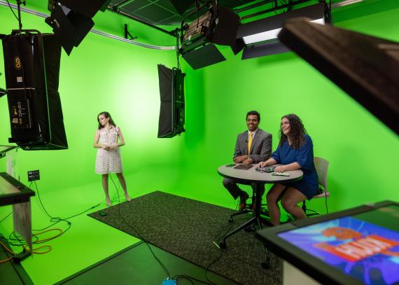 Students in front of a green screen anchor a news broadcast